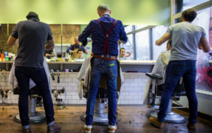 Rear view of three male barbers cutting hair in a salon.